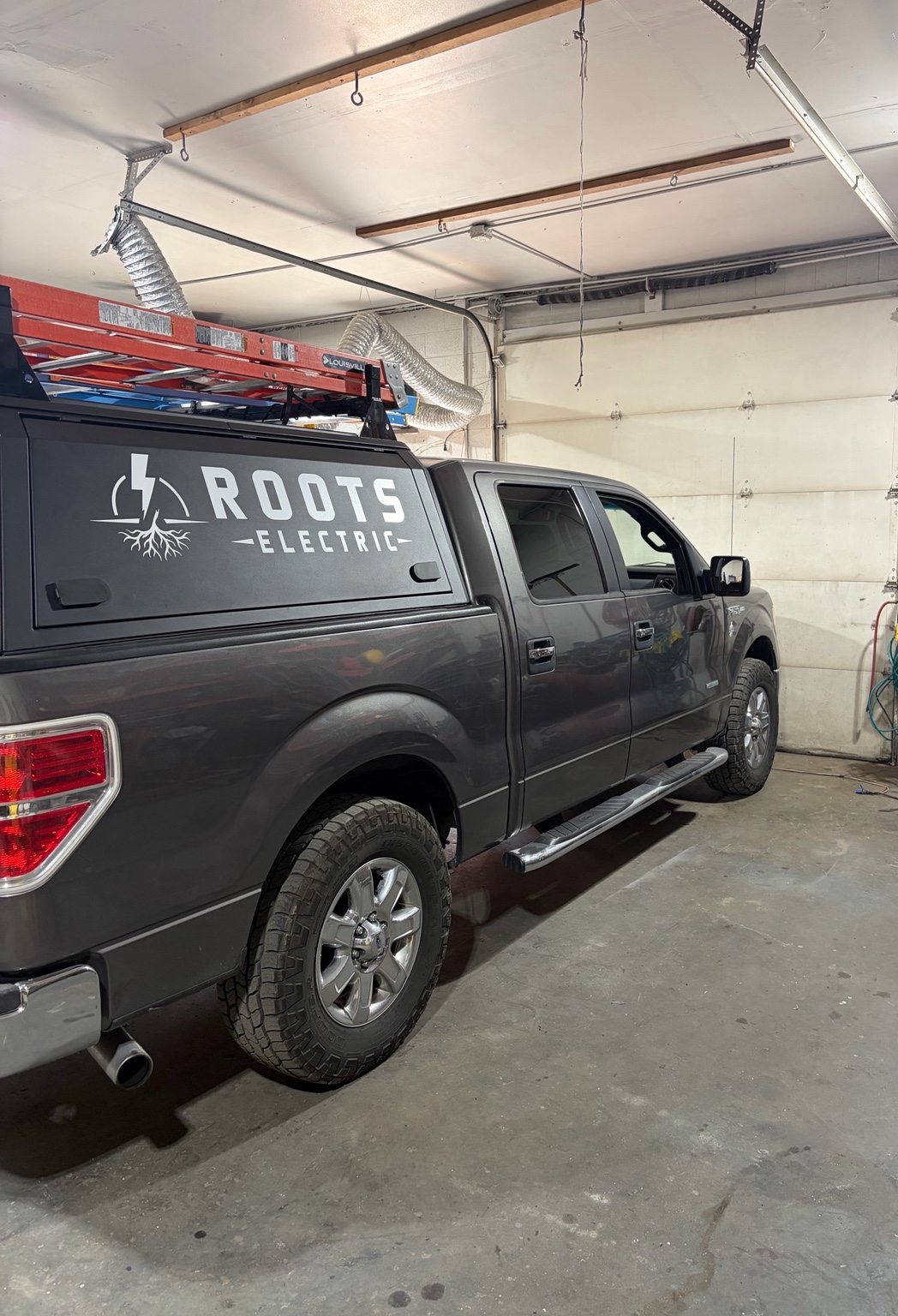 Gray pickup truck with the Roots Electric logo on the tailgate, parked in a garage