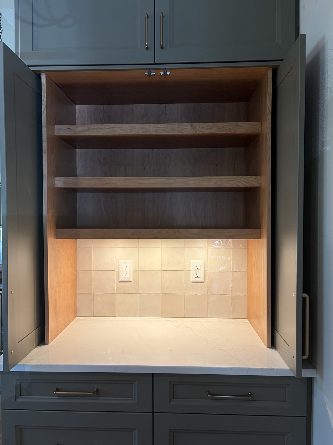 Open cabinet with warm lighting under wood shelves and a tile backsplash