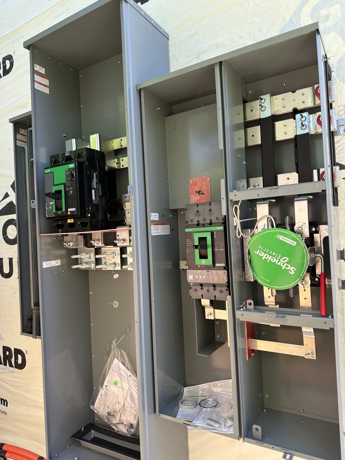 Open metal electrical service enclosures showing breakers, meter socket hardware, and bus bars on an unfinished exterior wall